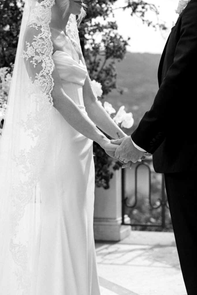 Black and white close-up of bride and groom holding hands during the ceremony