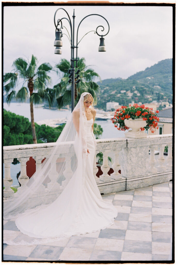 Film photograph of bride standing on a balcony overlooking Santa Margherita Ligure, veil trailing on the tiled floor