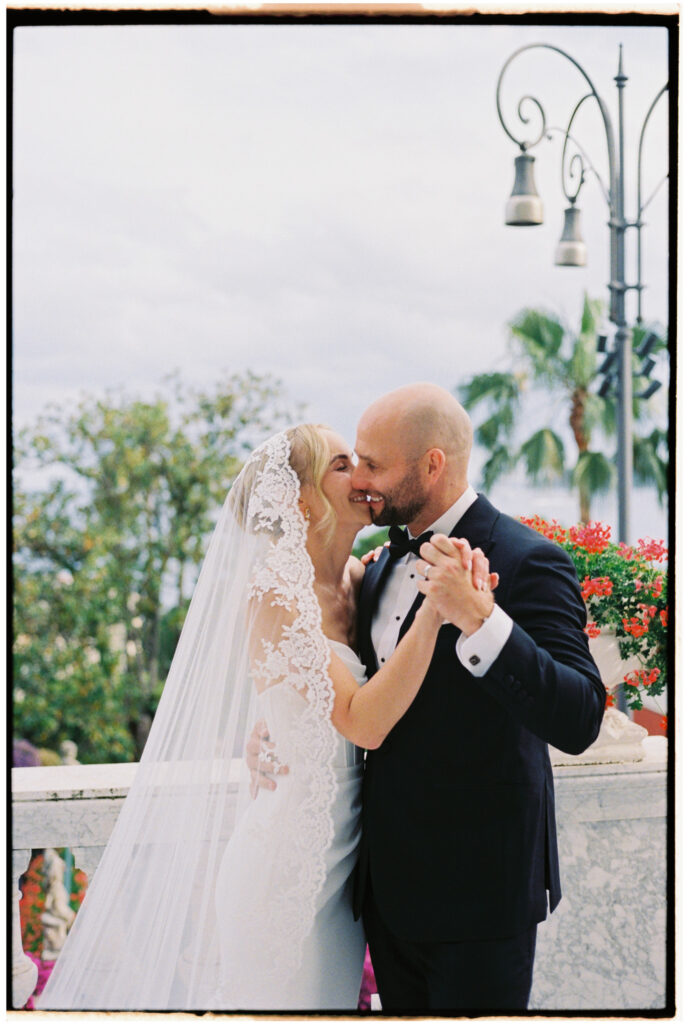 Film photograph of bride and groom dancing cheek to cheek on a balcony with palm trees and red flowers