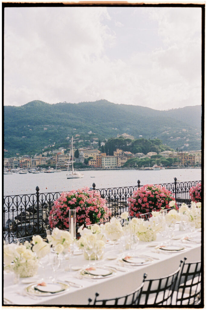 Film photograph of a reception table with cascading white floral arrangements and a view of the harbor and coastal town