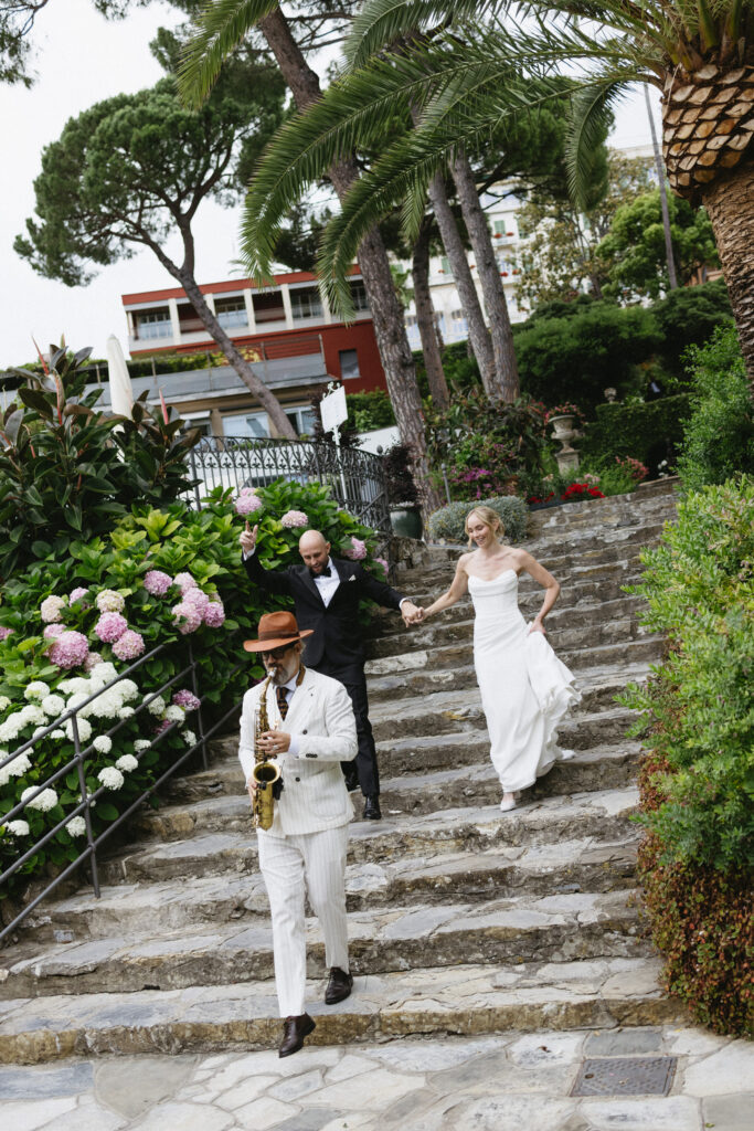 Bride and groom walking down garden steps led by a saxophonist, Imperiale Palace Hotel wedding reception