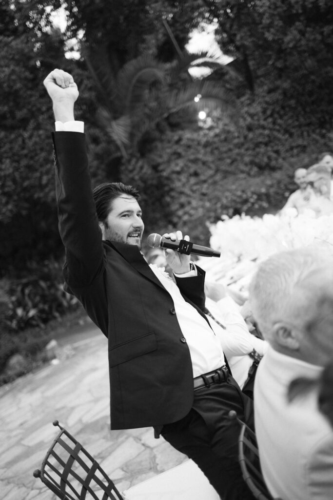Black and white photo of a wedding guest giving a toast with raised fist and microphone