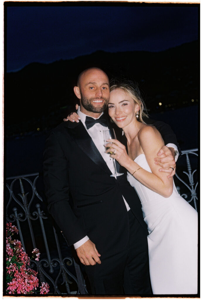Film photograph of bride and groom smiling close together at night, groom holding a champagne flute