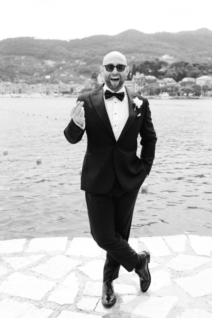 Film photograph of groom in tuxedo laughing and mid-stride on a stone terrace by the sea